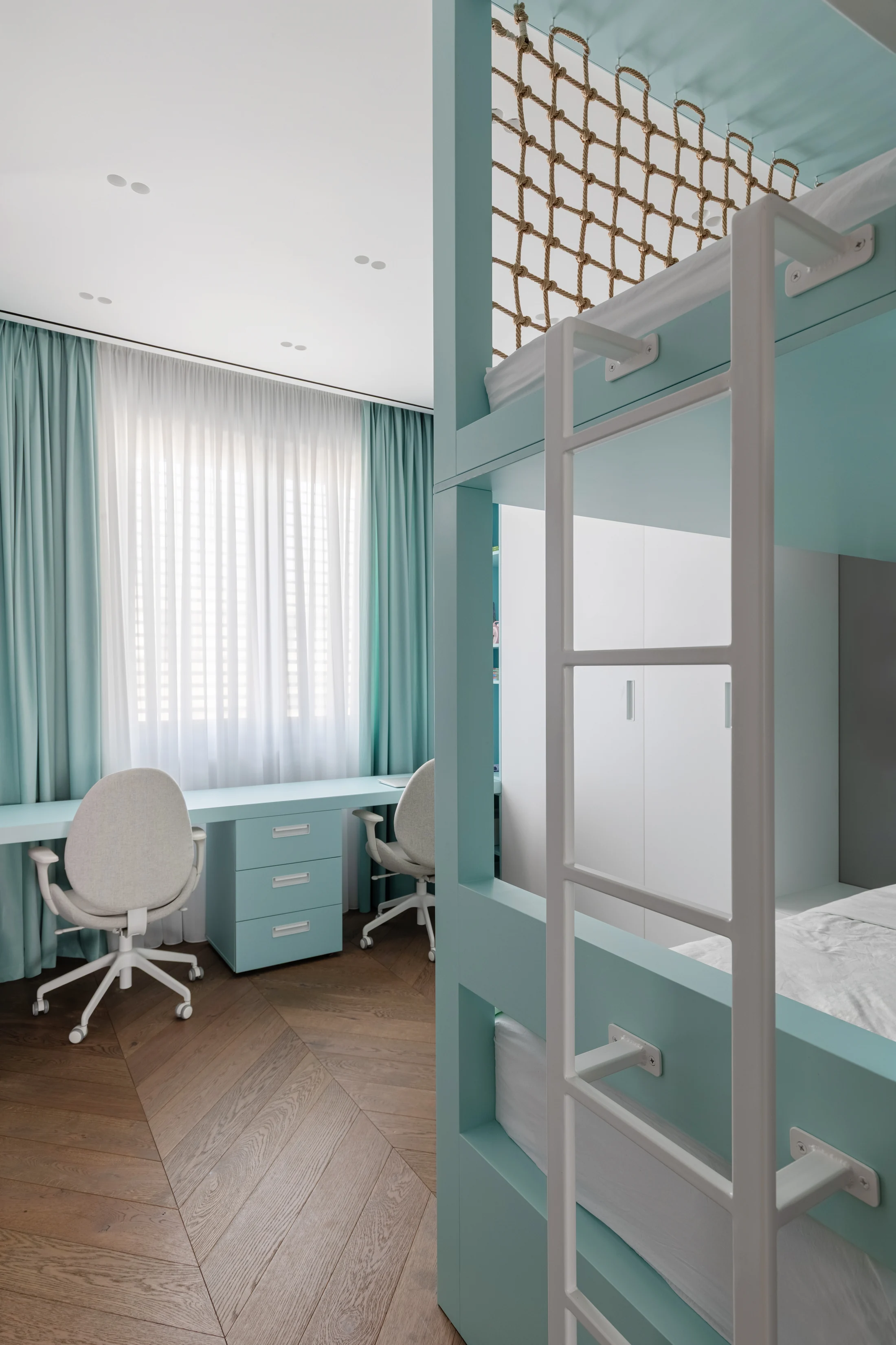 Birou cu sertare lângă fereastră, în spatele unui pat suprapus verde pal