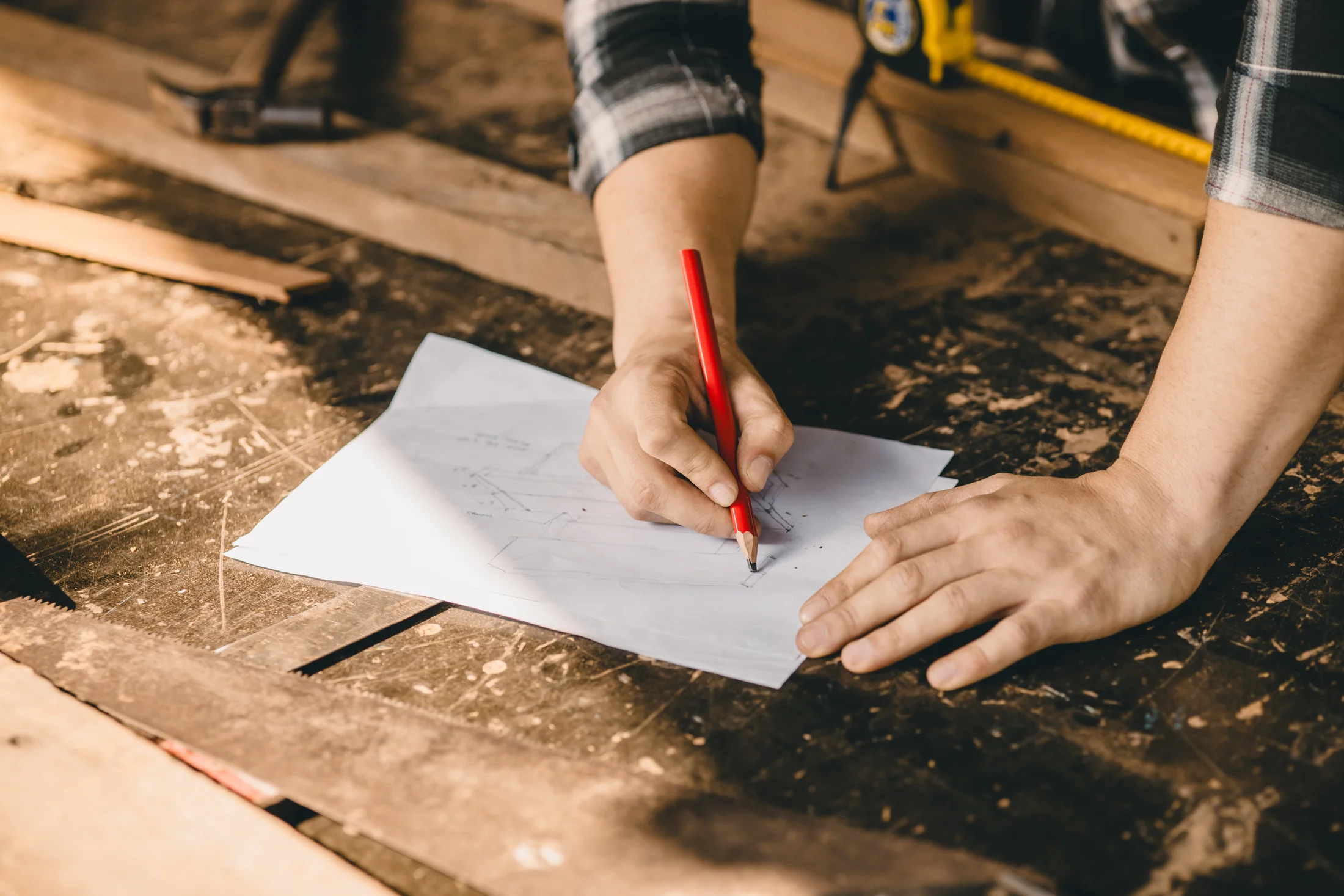 Mâini care schițează o piesă de mobilier pe bancul de lucru