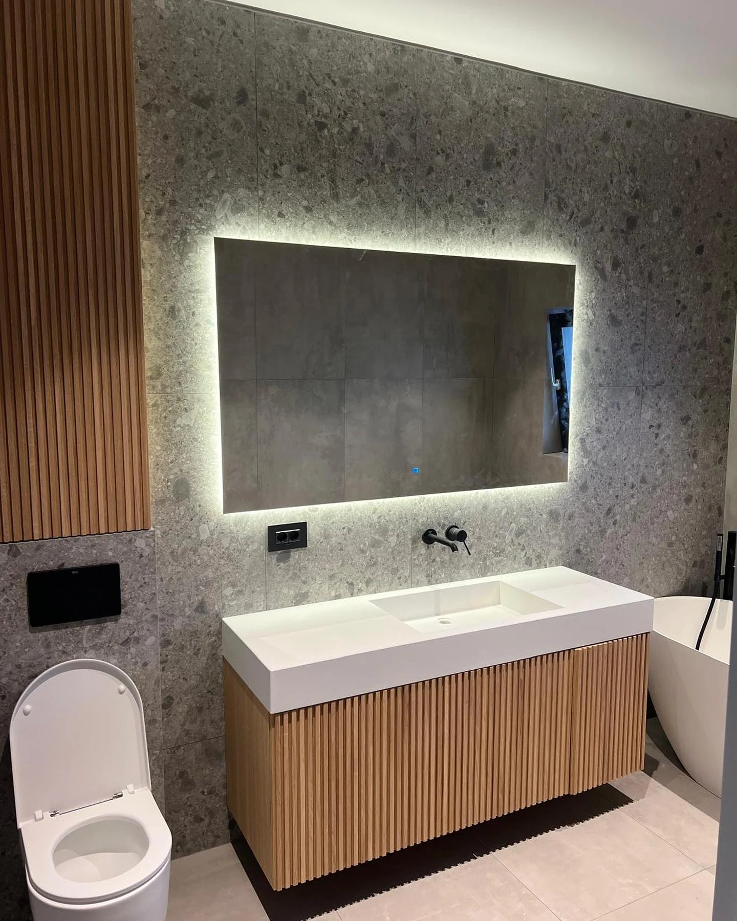 Mobilier pentru lavoar cu fronturi striate din lemn, alături de un corp suspendat cu același ritm vertical